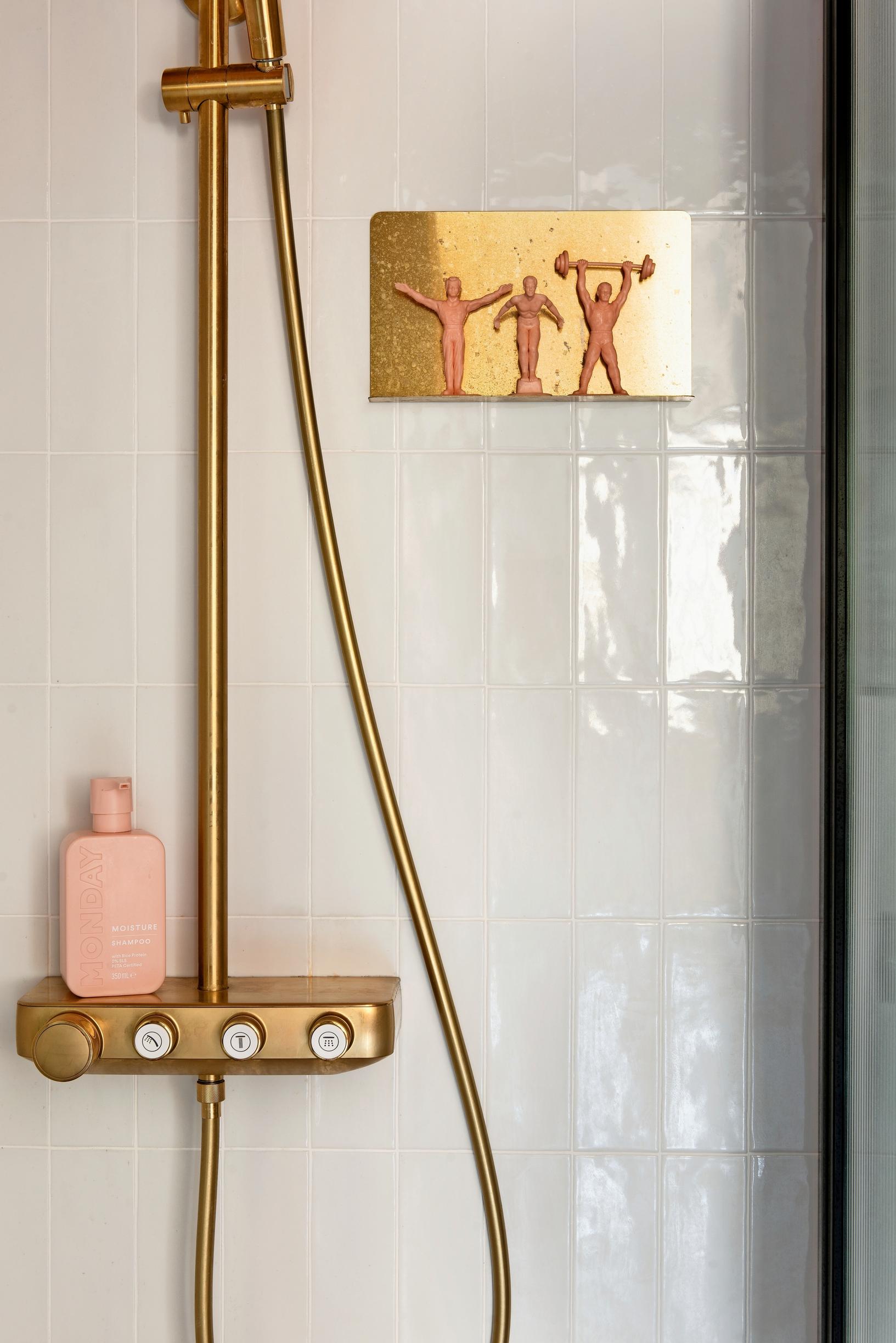 Grohe's brass shower and faucet in a white shower area.
