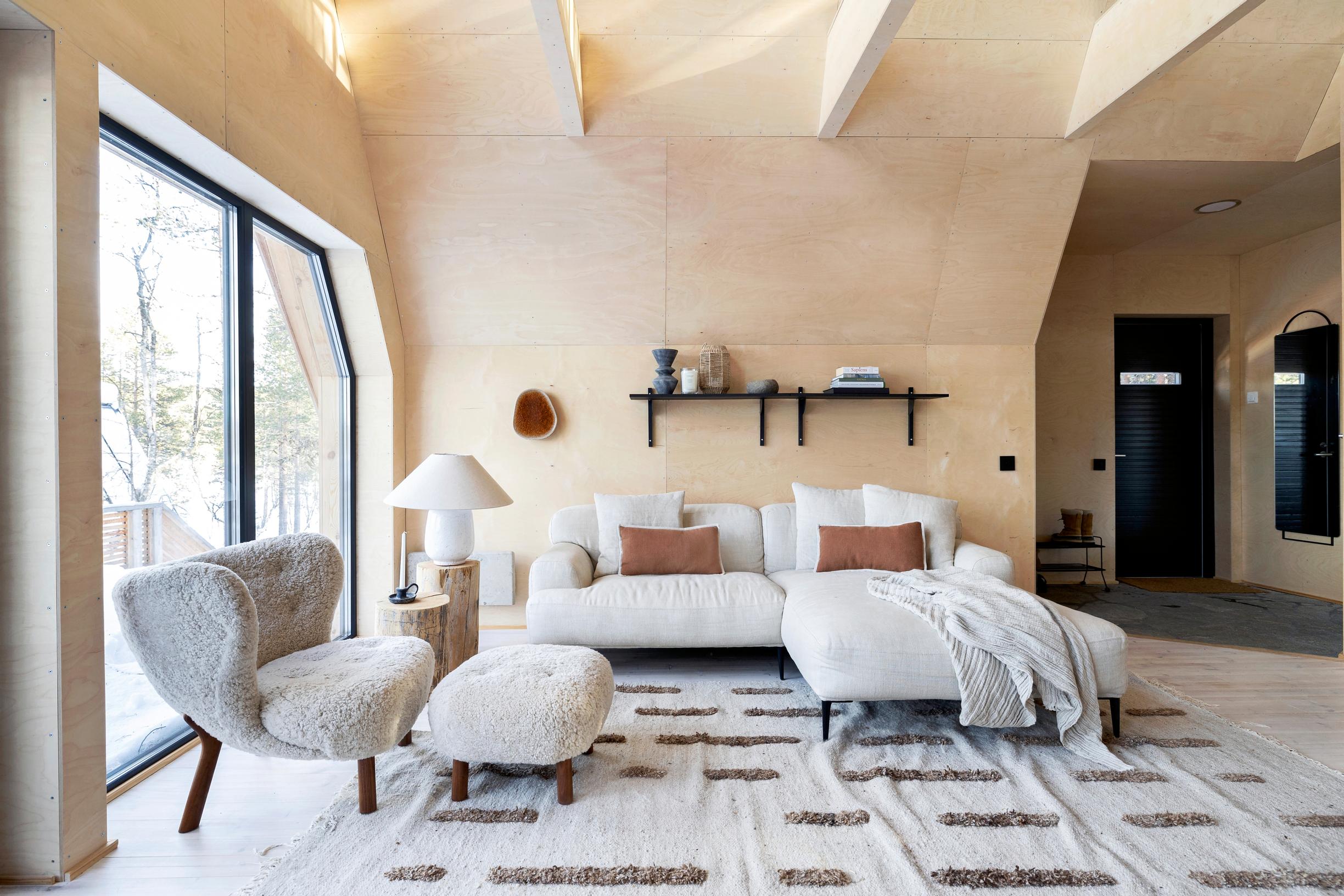 A plush modular sofa and nest-like armchair in the birch plywood-walled living room