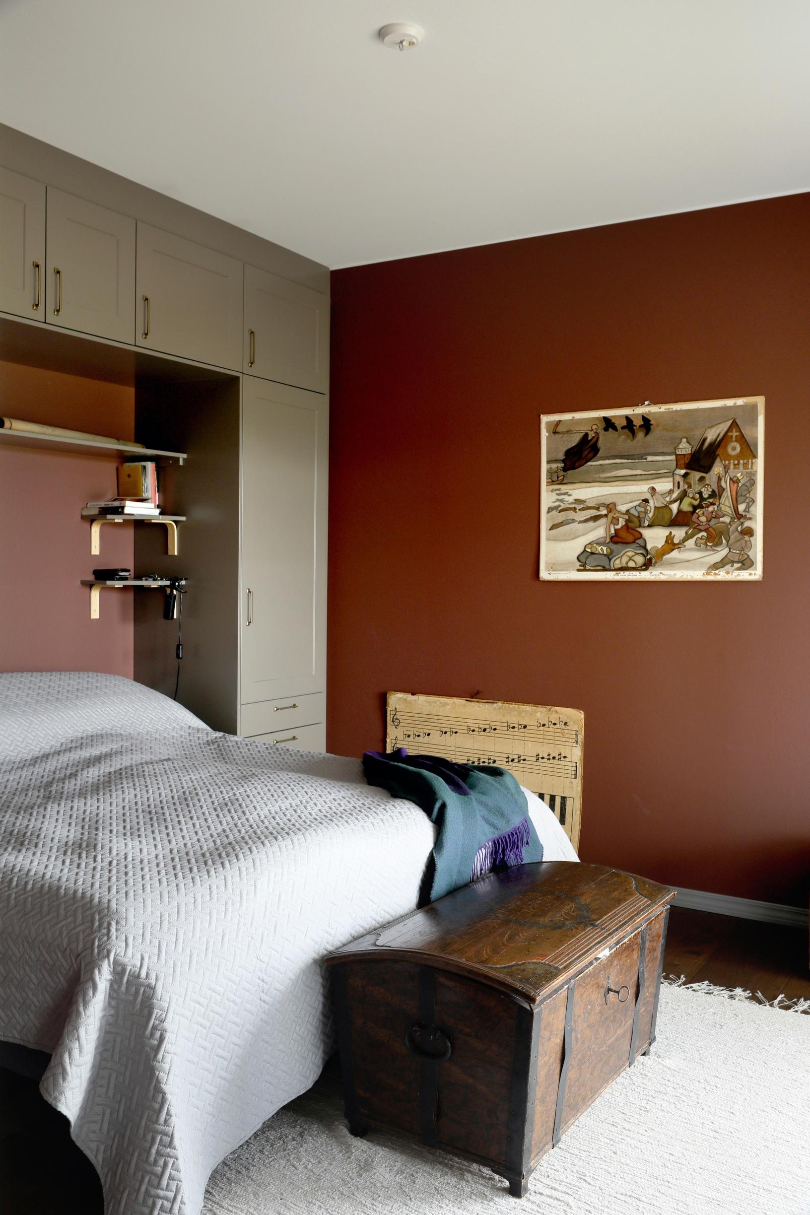 Bedroom with maroon walls and gray cabinets around the bed.