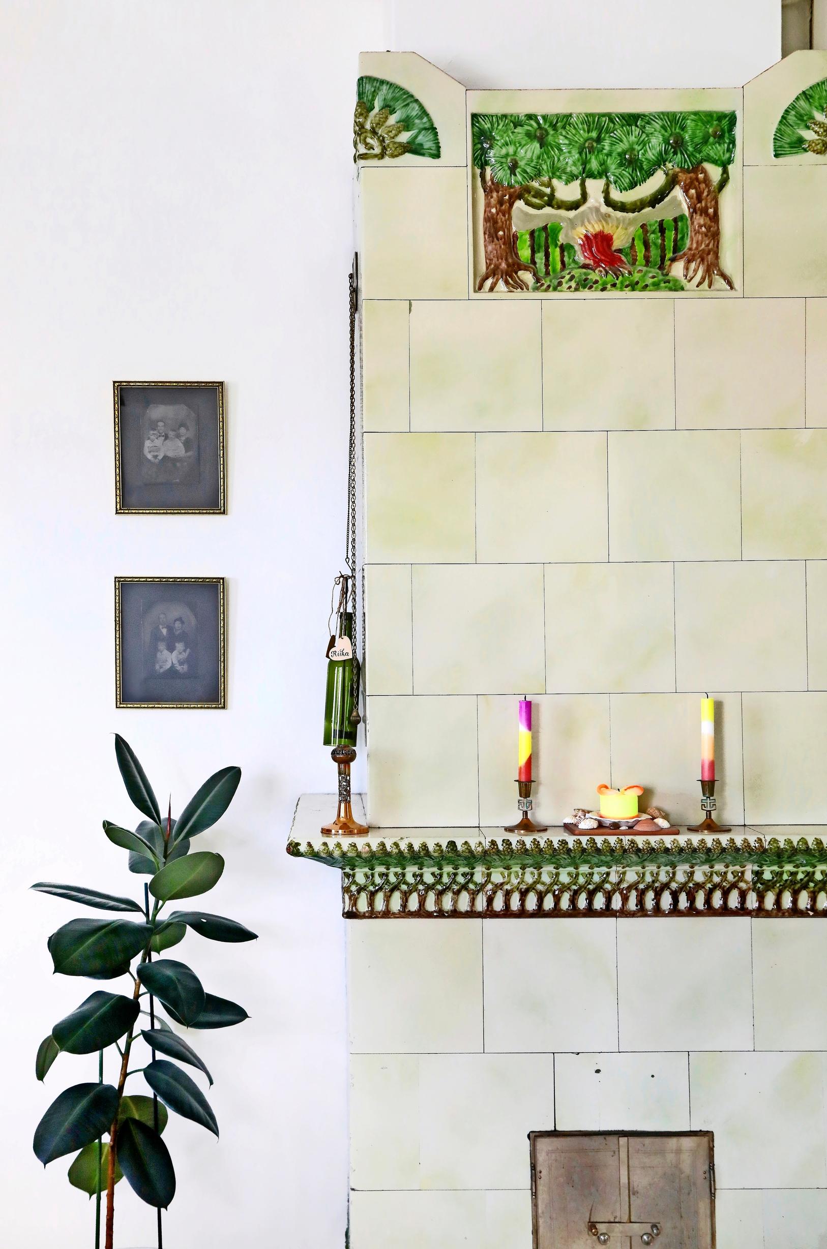 green-toned Mäntyuuni, candles, framed artwork, and a houseplant on the floor