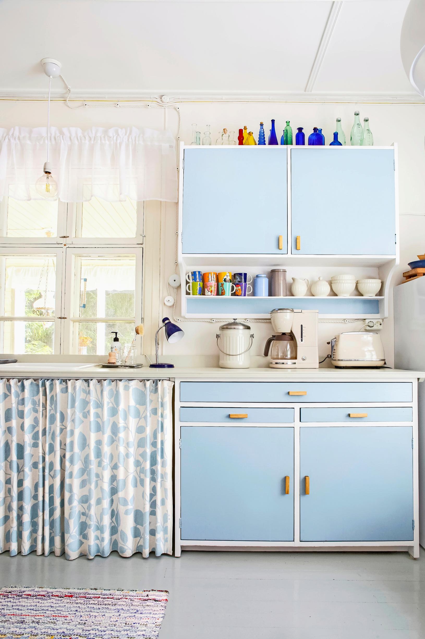 A curtain partially replacing lower cabinets in a nostalgic blue kitchen