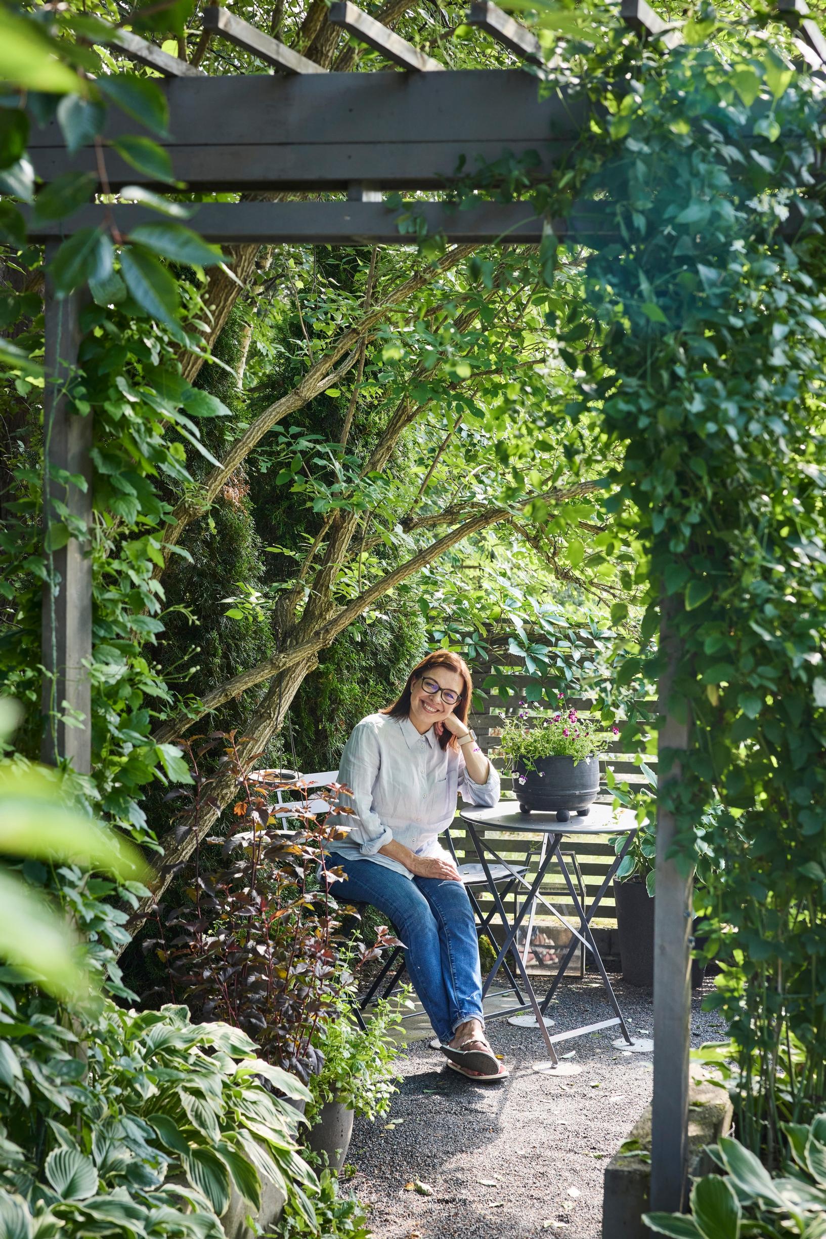 An arched trellis and seating area, with a woman seated.