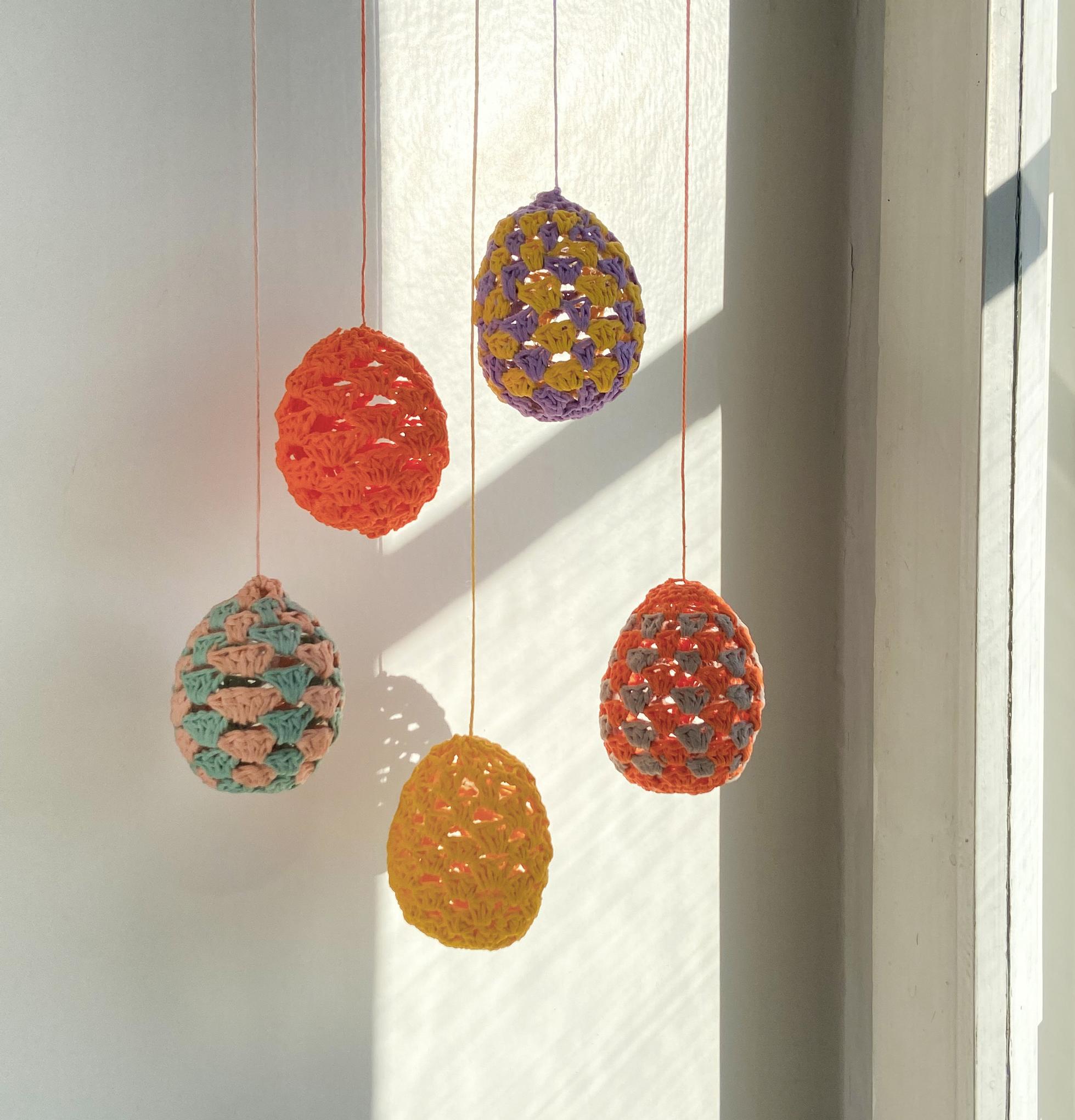 Crocheted Easter eggs hanging in front of a window.