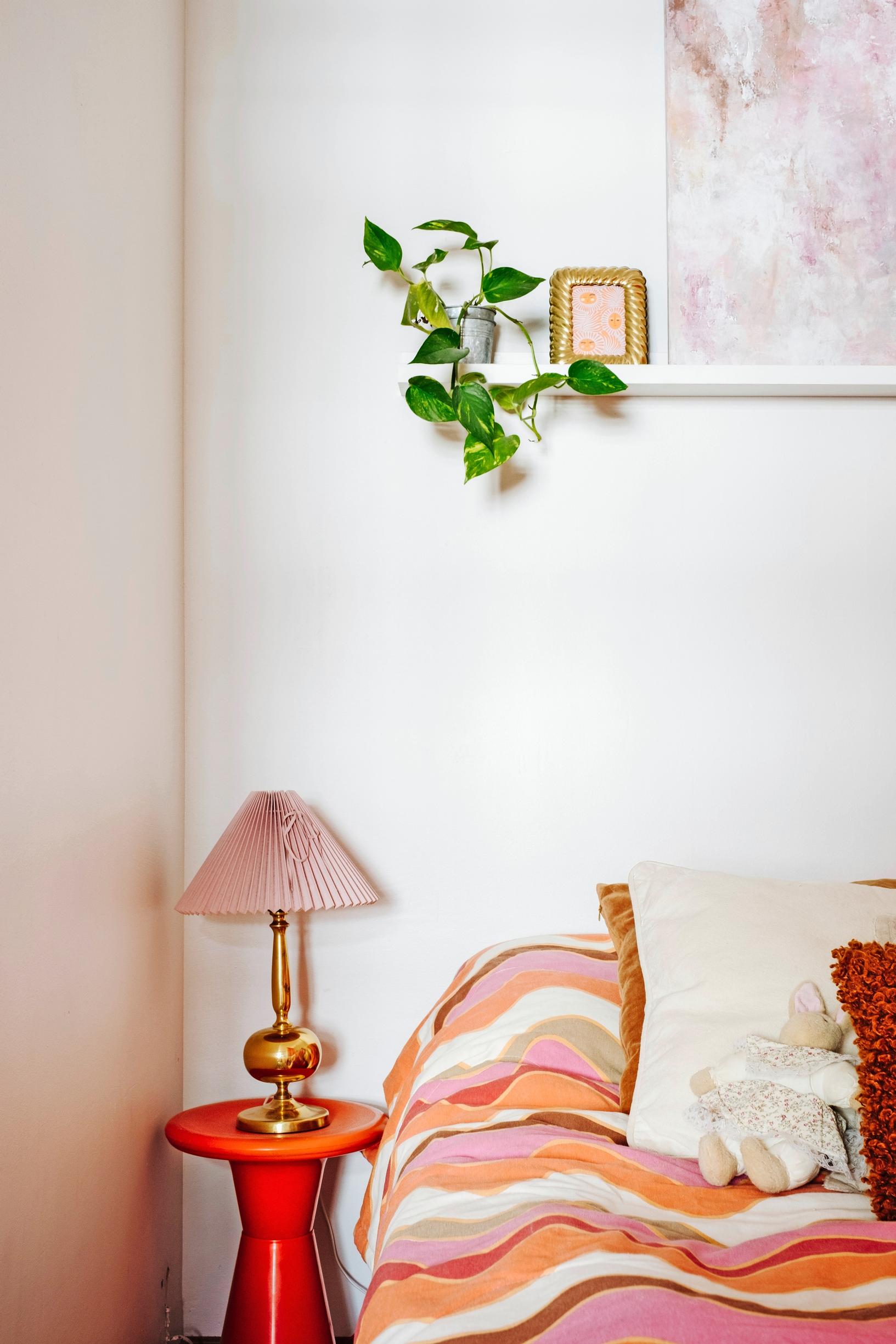 Photo of a bedroom corner with a red plastic nightstand and an old table lamp.