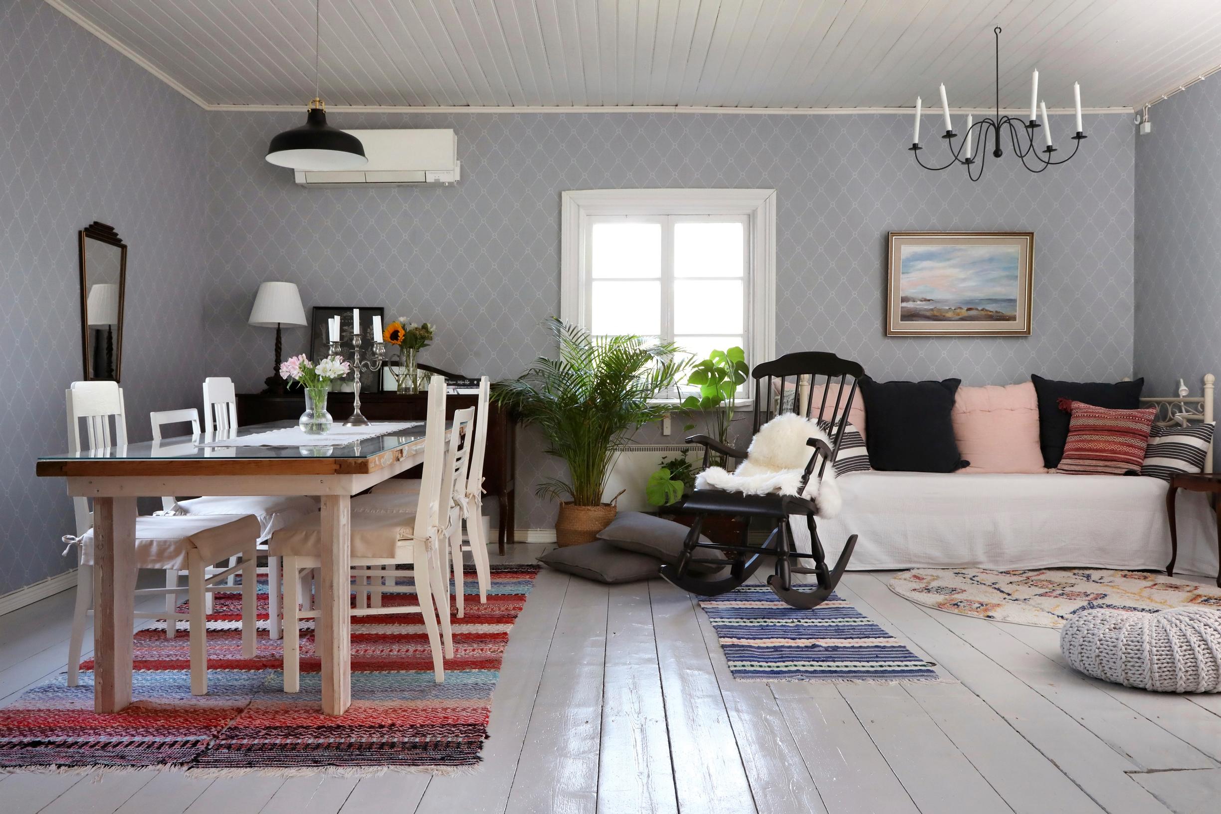 A living room with a table setting, rocking chair, sofa, ottoman, painting, rag rugs, and plank floor