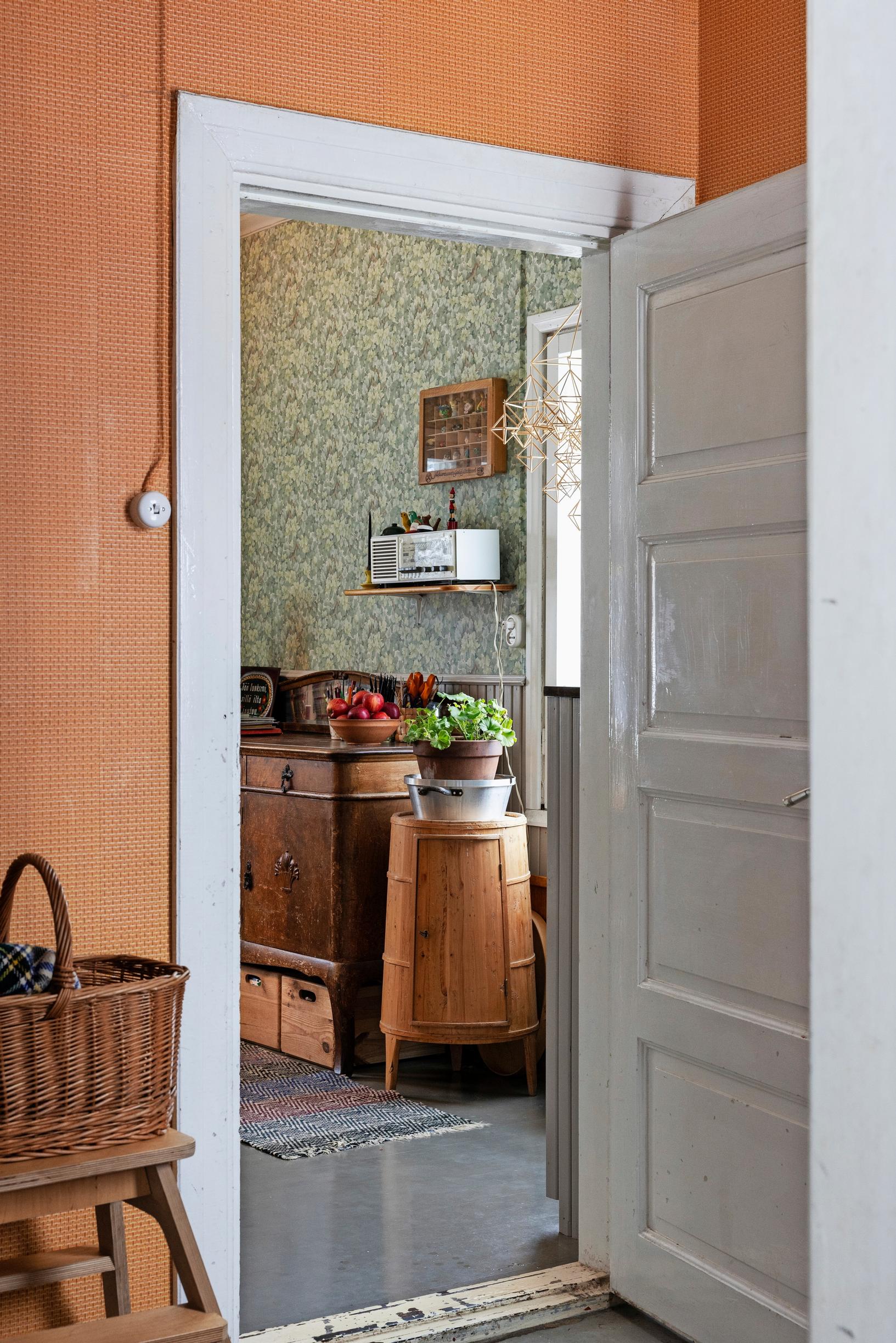 Basket on the kitchen step, open paneled door to the living room with a dresser and green wallpaper