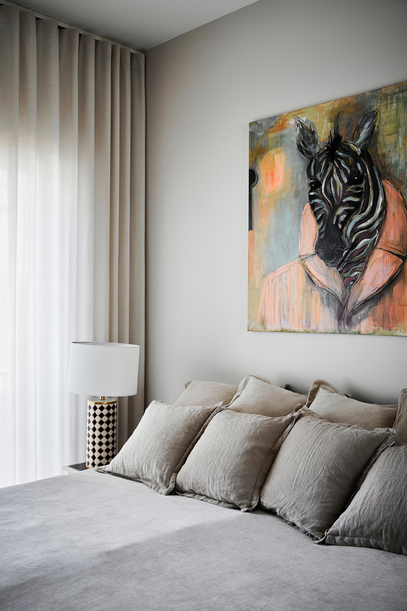 A bedroom with a made-up bed and a painting featuring a zebra’s head.