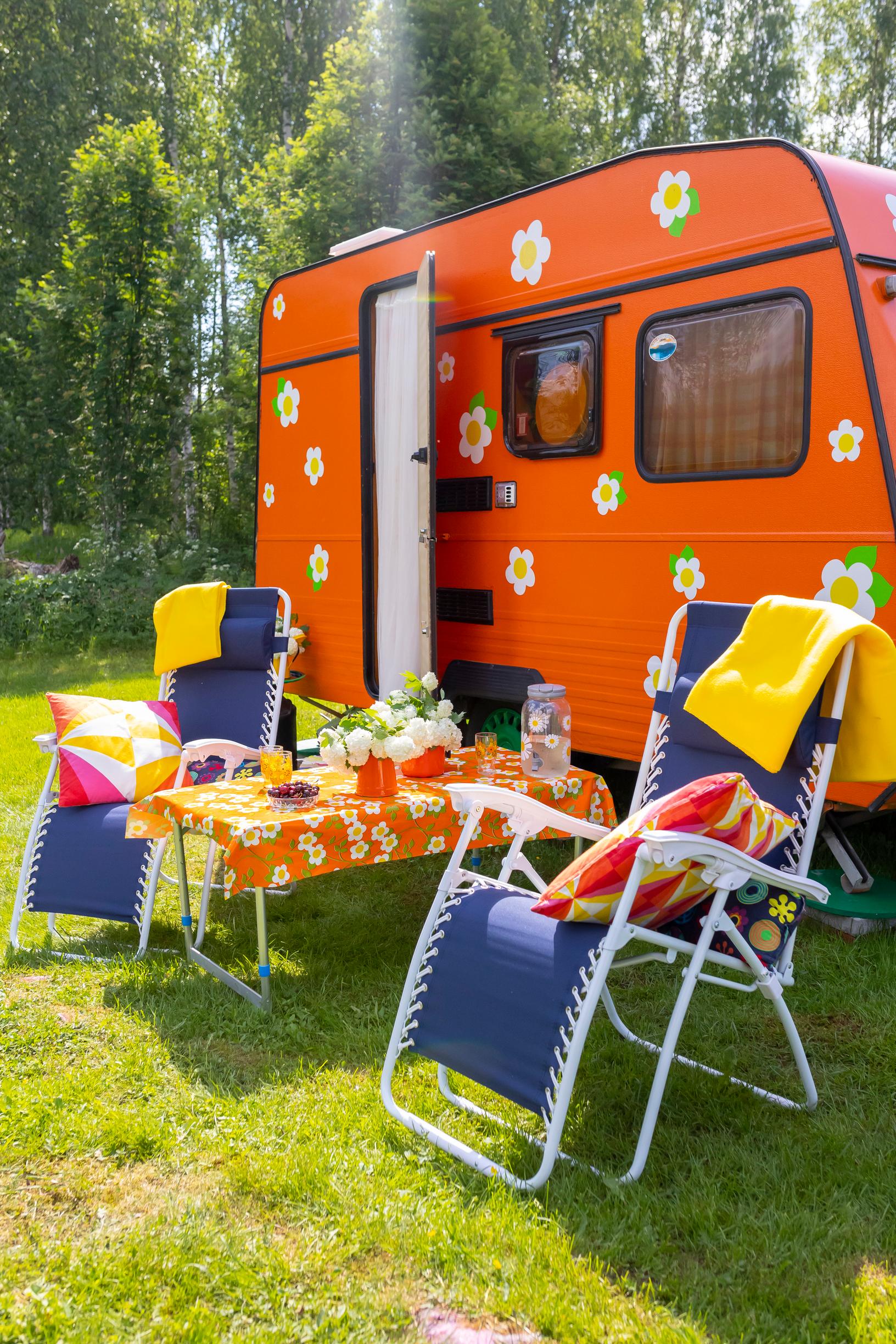 an orange travel trailer, blue lawn chairs, and a table set in the garden