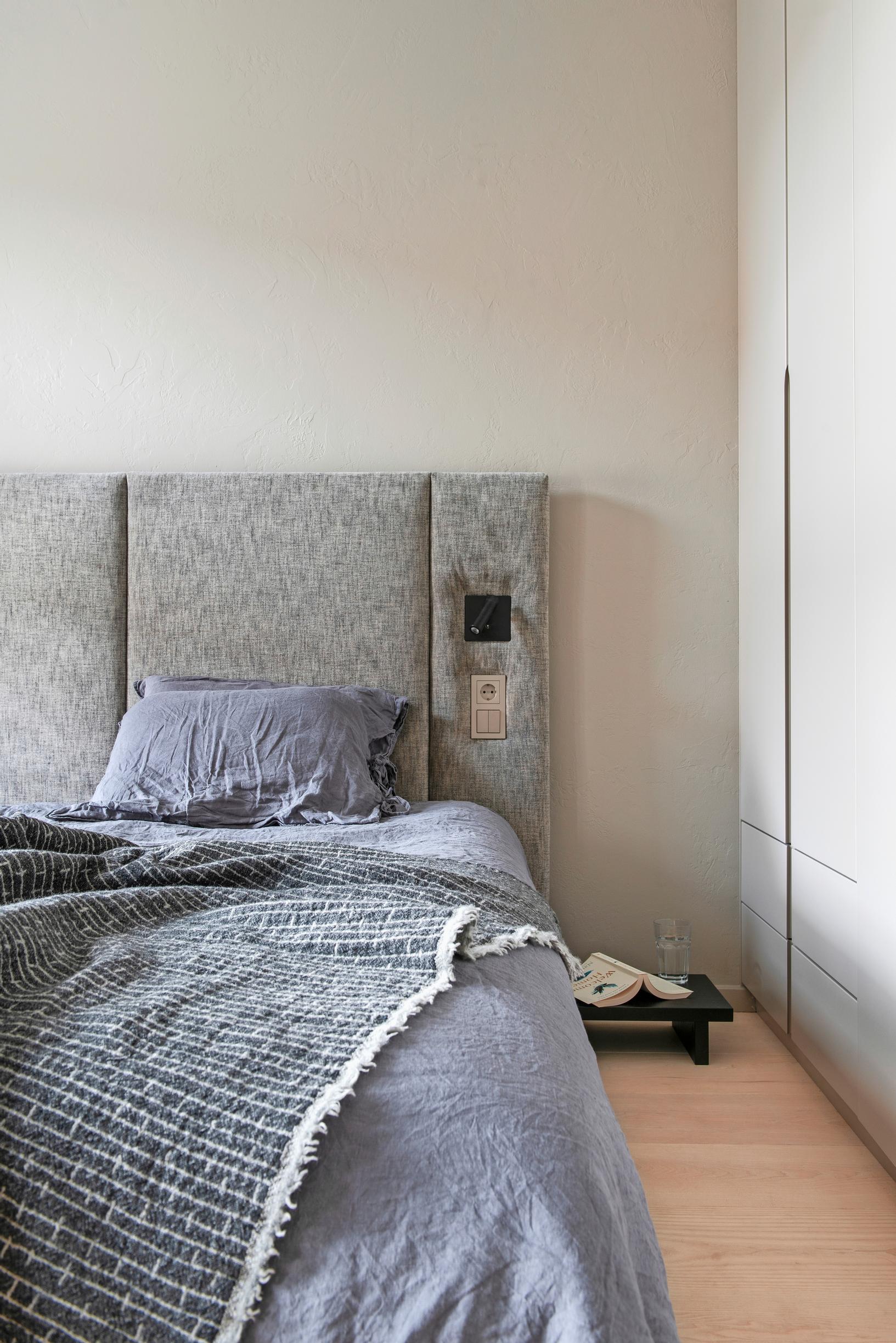 A custom gray headboard and a wardrobe with finger-pull handles in the bedroom