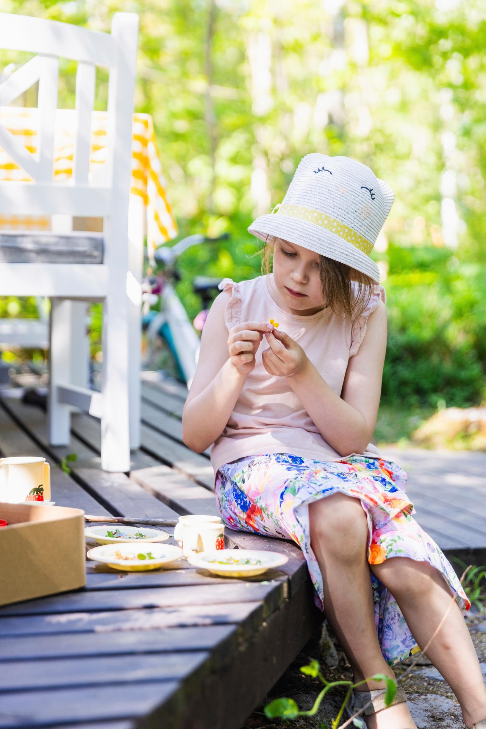 a girl sits, examining something, on a summer terrace