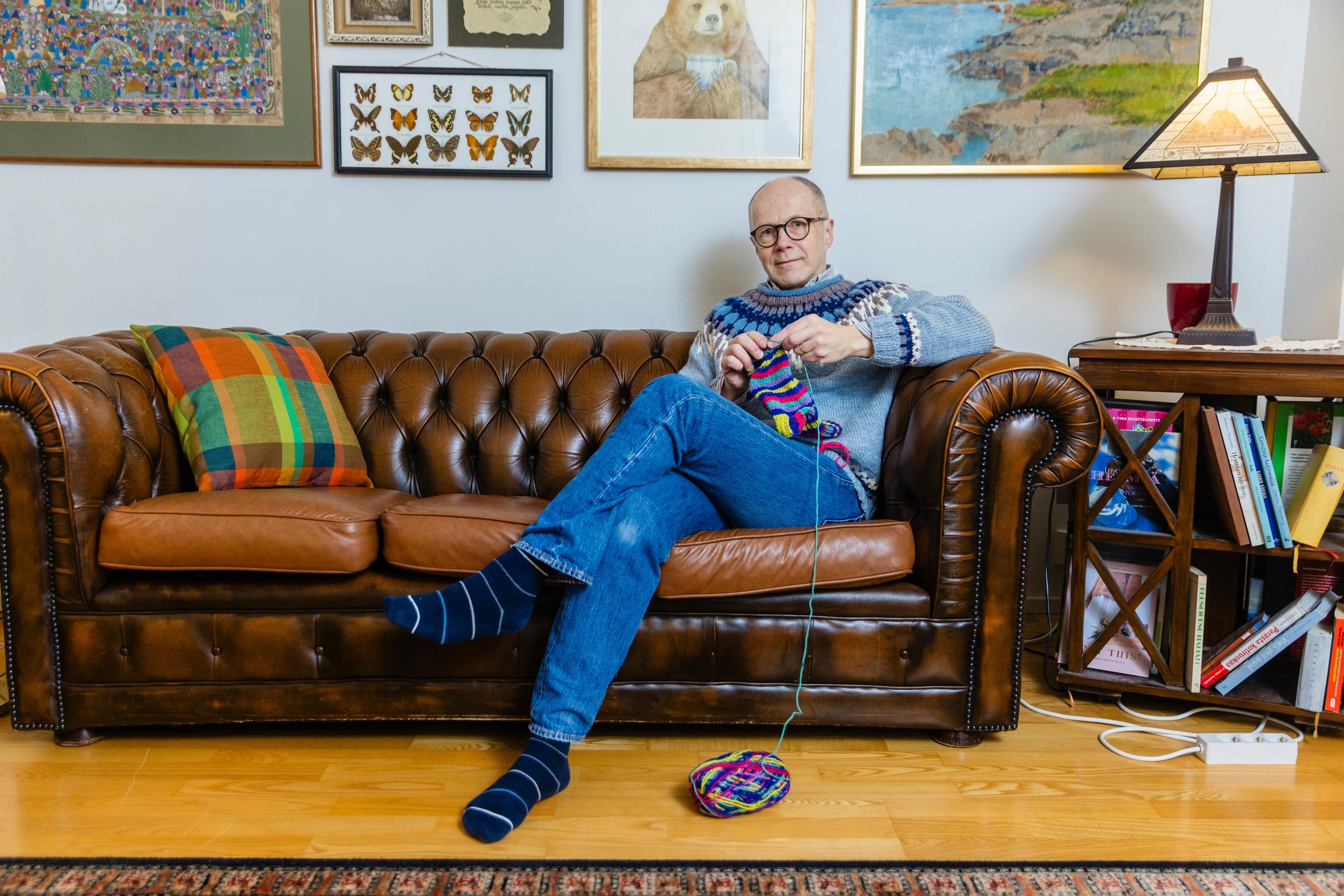 man sitting on a leather couch, knitting