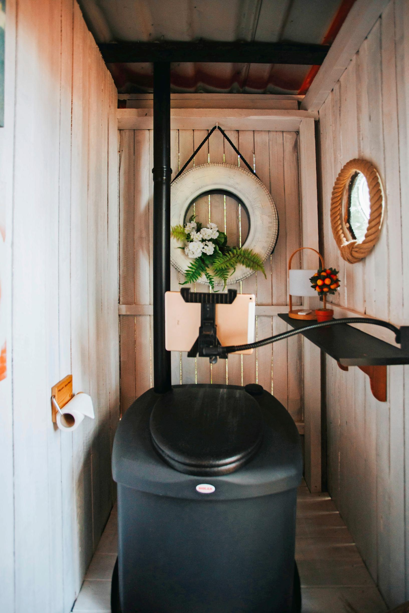 A look at the outhouse interior: a composting toilet, white walls, and a decorative piece made from a car tire.