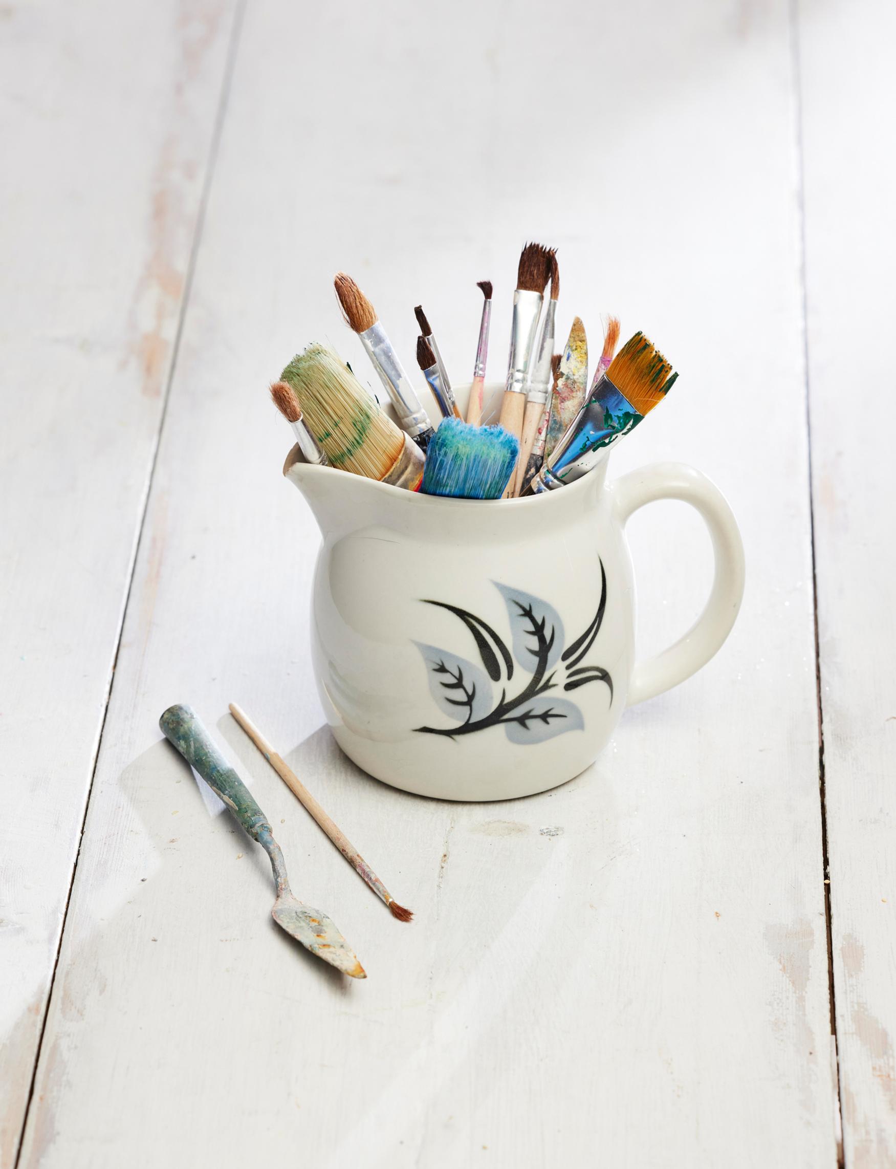 An old Arabia milk pitcher holding paintbrushes.