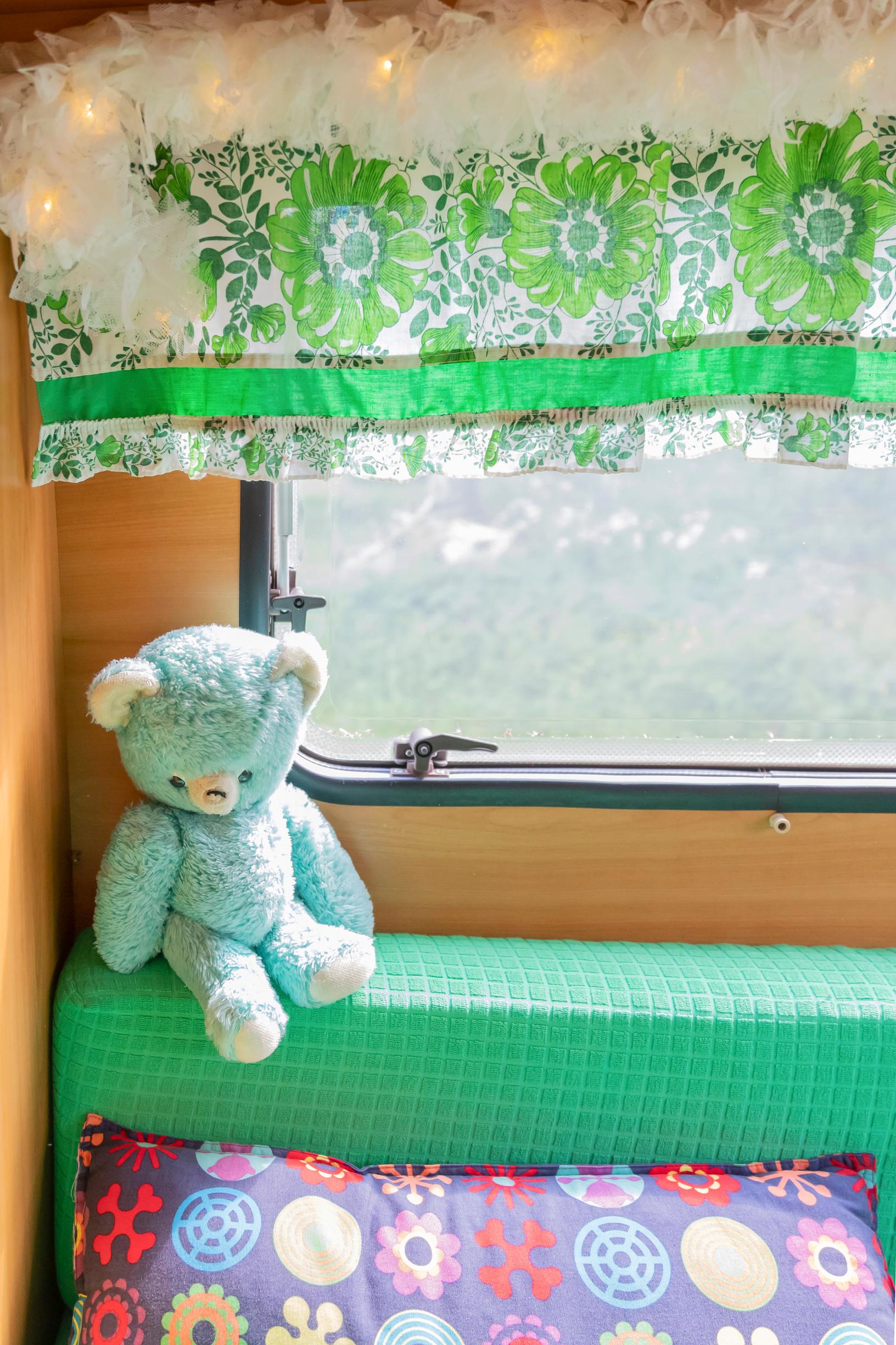 an old teddy bear on the trailer’s sofa, retro curtains, and a colorful throw pillow