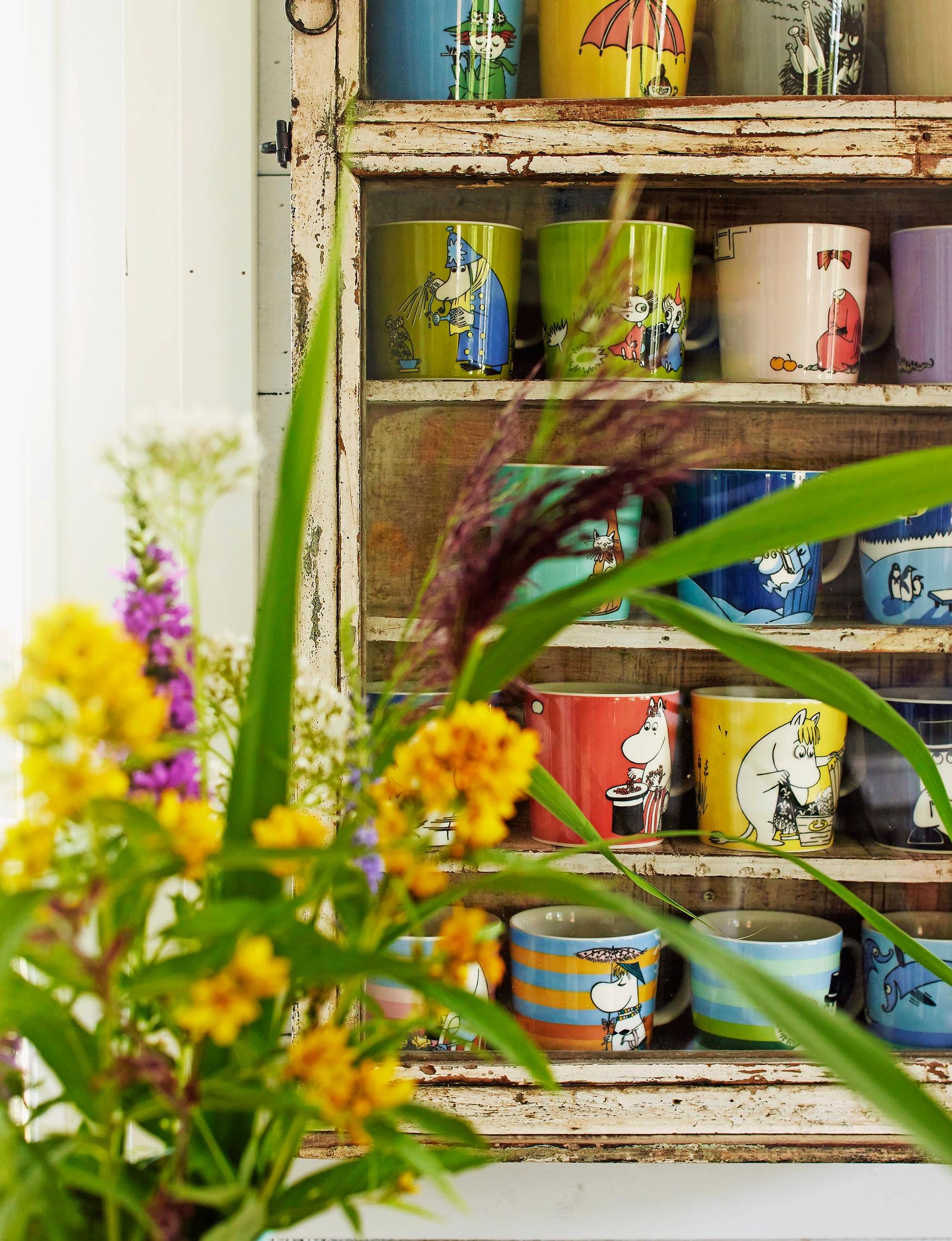 summer flowers in a vase and Moomin mugs on the shelf